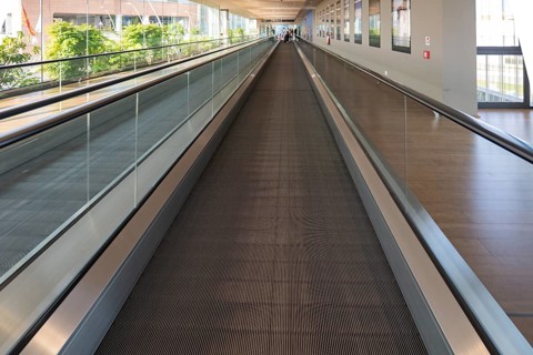 A modern airport travelator extends into the distance, surrounded by glass walls and natural light.