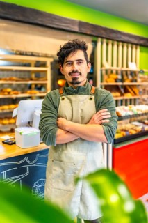 Vertical portrait of a latin male artisan baker standing proud in the shop of new business