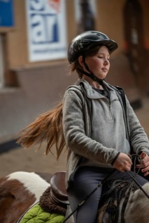 Little girl, 10 years old, in the saddle on a horse in an indoor riding arena,