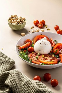 A vibrant salad featuring creamy burrata, juicy tomatoes, and crunchy pistachios. Served in a white
