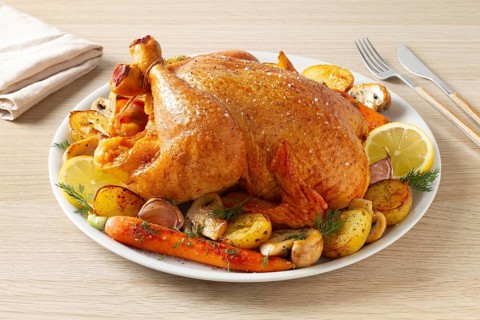 A golden-brown roasted whole chicken is served on a white plate with roasted potatoes, carrots,