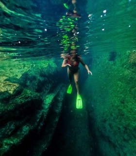 Underwater view of a woman with flippers snorkeling in the crystal clear waters of a natural pool