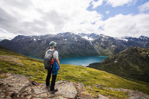 Adventurer stands on a rocky ridge, overlooking a serene turquoise lake surrounded by Norway's