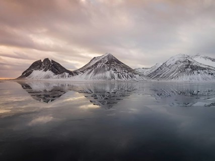Captivating view of Iceland's Stokksnes mountains reflecting on the calm, icy waters. Snow-dusted