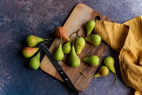 A collection of wild pears is artfully arranged on a rustic wooden cutting board. The setting