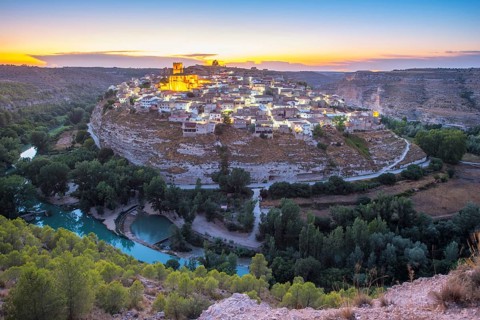 A breathtaking view of the historic town of Jorquera, Spain, perched on a cliff at sunset. The
