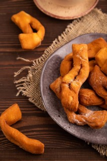 Crunchy biscuit Brushwood cookies sprinkled with powdered sugar on brown wooden background and