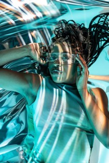 Young African woman immersed in a futuristic metaverse setting, wearing clear high-tech glasses