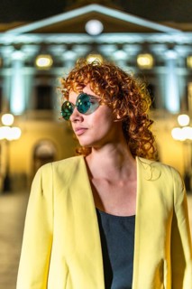 Vertical photo of a distracted modern woman in sunglasses and yellow jacket in the city at night