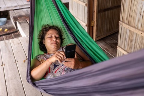 A mature woman enjoys a tranquil moment in a vibrant green hammock on Kri Island, Raja Ampat, while