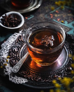 A warm glass cup of tea infused with anise, set on an intricately designed metal tray. The aromatic