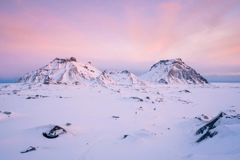 A breathtaking view of Katla Glacier's rugged snow-covered mountains beneath a pastel pink sunrise