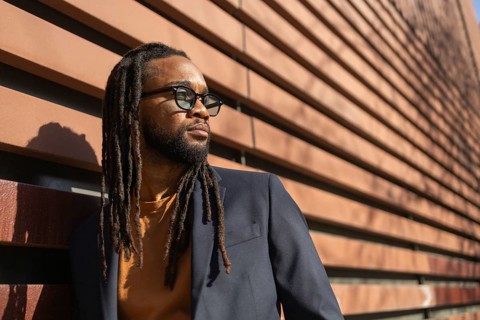 A cuban business man with sunglasses leans against a modern wall in sunlight, showcasing a blend of