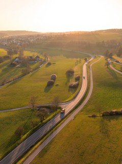 Winding country road through green fields and trees, under a warm sunset sky, Gechingen, district
