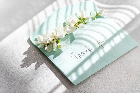 Top view of delicate spring snowdrops arranged on a pastel thank you card, with natural sunlight