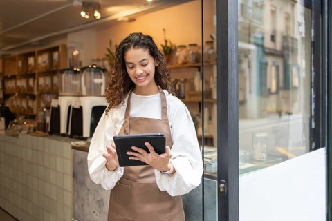 A smiling clerk wearing an apron uses a tablet to manage inventory at an organic bulk store.
