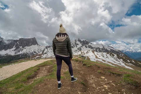 A woman stands at Passo Giau in the Dolomites, Italy, gazing at the snow-covered mountains under