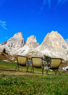 Three camping chairs in a meadow at Passo Sella in front of dramatic mountain peaks under a clear