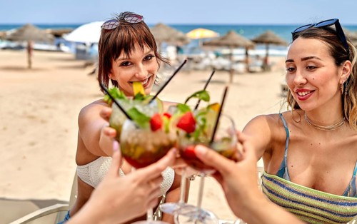 Friends gather on a sunny beach, enjoying colorful cocktails while celebrating summer. Laughter and
