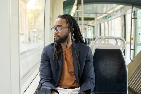 A cuban business man sits thoughtfully on a modern tram, gazing out the window. The serene