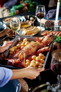 Cropped unrecognizable woman's hands serving a roasted suckling pig accompanied by potatoes,