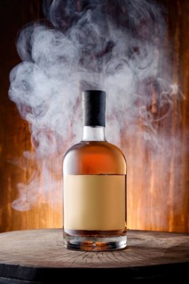 Bottle of blended malt smoked scotch whisky surrounded with smoke on wooden background