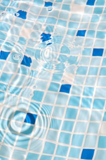 A close-up image of mosaic tiles under clear, rippling water, creating a serene and refreshing