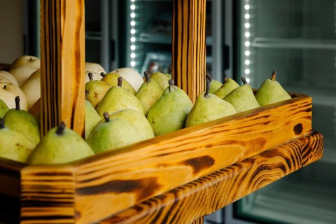 Fresh green pears neatly arranged in a rustic wooden display case at a market in Tulum, Mexico. The