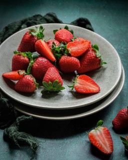 A collection of ripe, red strawberries on a ceramic plate, some halved to show their juicy interior
