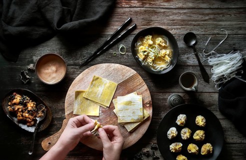 Top view of anonymous woman preparing wonton soup on a wooden table