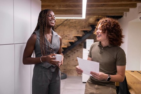 Two coworkers enjoy a lighthearted conversation in a modern office setting, fostering a positive