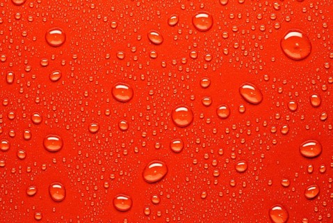Close up of water droplets on a bright red surface, capturing the texture and varying sizes of the