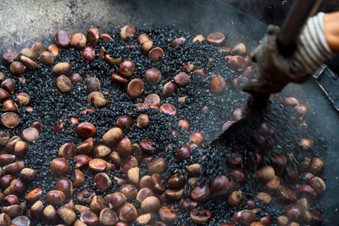 Close-up view of a cropped unrecognizable person roasting fresh chestnuts in a large pan at a Hong