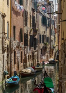 Narrow canal between tall old buildings, lined with boats in a quiet, historic neighbourhood,