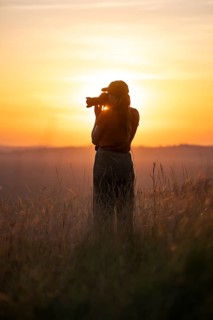 Young woman taking pictures at sunset, standing in tall grass, Lake Victoria, Uganda