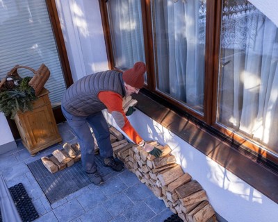 A senior man in casual winter wear stacks eco-friendly firewood next to his home on a clear day.