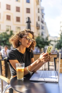 Vertical photo of a young Moroccan female freelancer working with mobile and laptop in a sidewalk