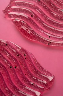 A detailed view of pink scrub and cosmetic gel, elegantly smeared on a pink surface, showcasing the