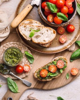 Rustic toasts topped with vibrant cherry tomatoes and fragrant pesto, presented on a wooden board.