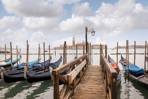 Scenic view of a wooden dock leading to gondolas in Venice, Italy. The background showcases the