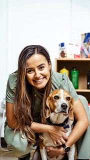 A nutritionist smiles warmly, embracing a beagle in an office setting. Shelves with nutritional