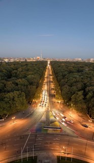 An aerial view of Berlin's Strabe des 17 Juni at dusk, featuring a tree-lined boulevard illuminated