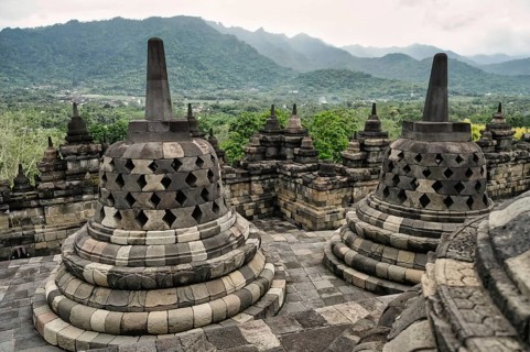 Majestic view of the Borobudur Temple's ancient stone stupas, with vibrant green mountains and lush