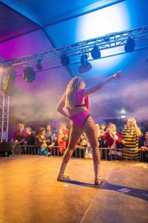 A dancer performs on a colourful stage in front of a celebrating audience, carnival, Schlagerkuchen
