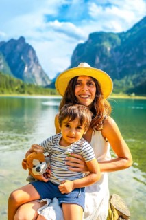 Mother holding her son while enjoying a sunny summer day at lake dobbiaco with the dolomites in the