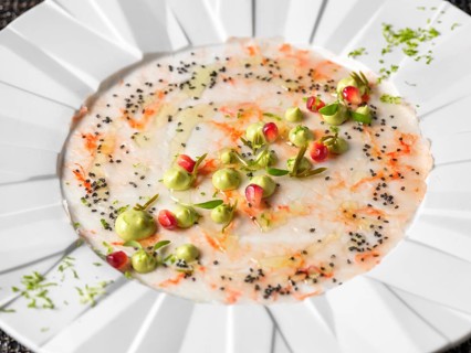 A beautifully arranged seafood carpaccio garnished with delicate green cream, red pomegranate