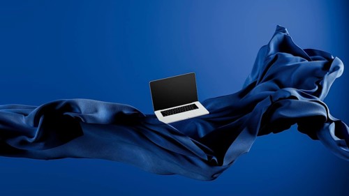 A sleek laptop is placed atop smooth fabric, showcasing its lightweight design against a rich blue