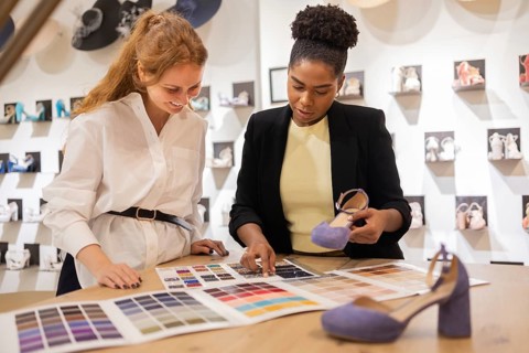 Two women discuss color options for footwear in a bridal studio. They review a color palette and
