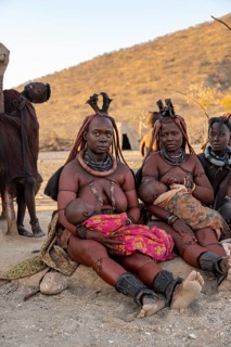 Married Himba woman with their babies in their arms sitting in front of the hut of the first woman,