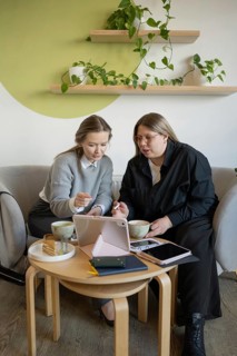 Two women engage in a collaborative discussion at a cozy cafe, using a tablet. They sit at a wooden